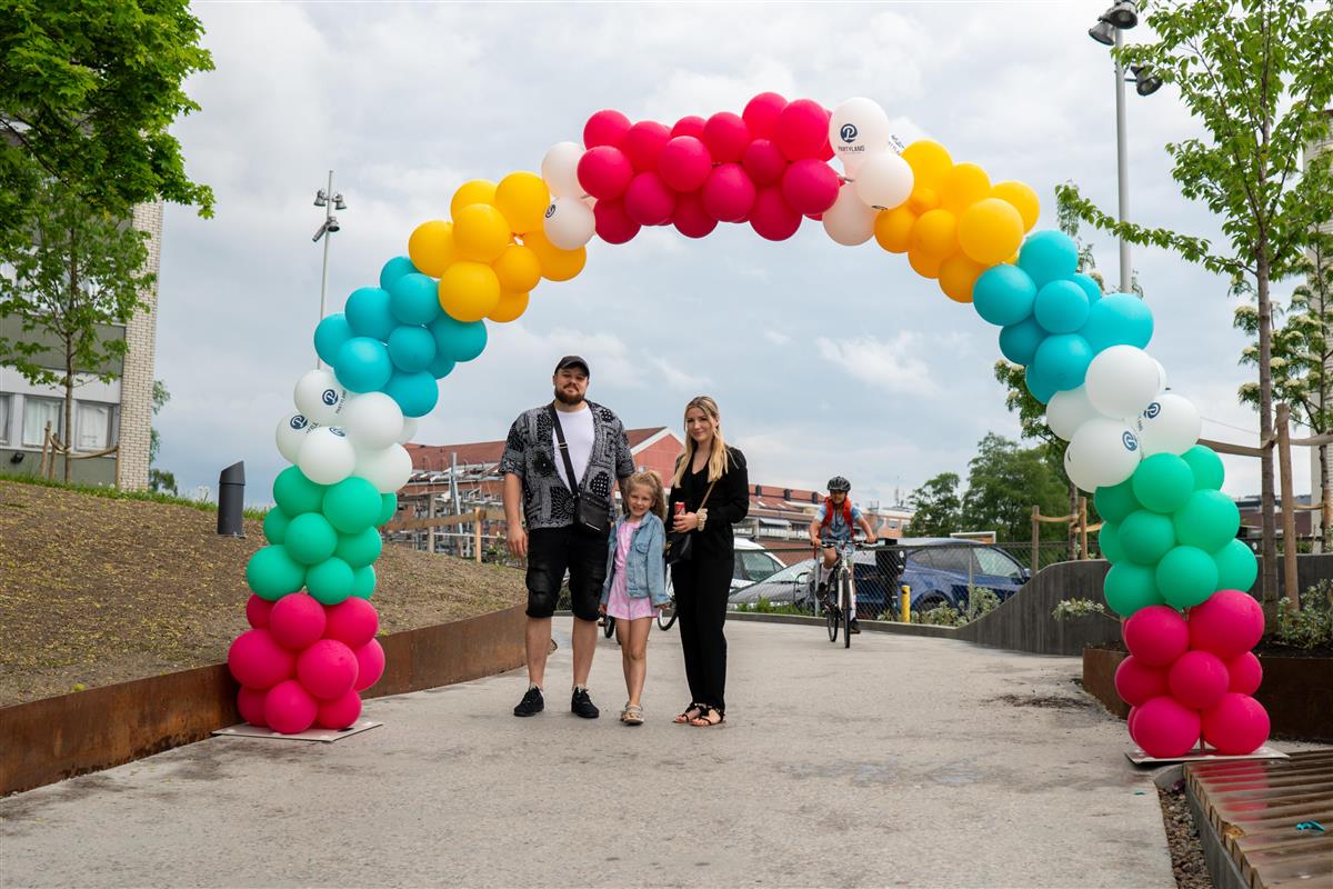 To voksne og et barn under en flerfarget ballongbue - Klikk for stort bilde