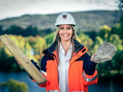 Dame i arbeidstøy og hjelm som hålder byggematerialer - Klikk for stort bilde