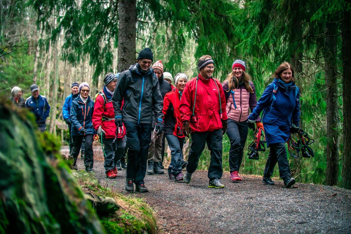 En gruppe mennesker går tur på grusvei i skogen - Klikk for stort bilde
