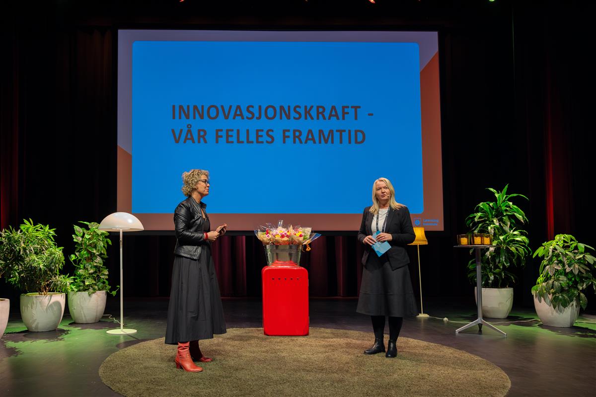 To personer står på scene foran skjerm som sier "Innovasjonskraft - vår felles framtid - Klikk for stort bilde