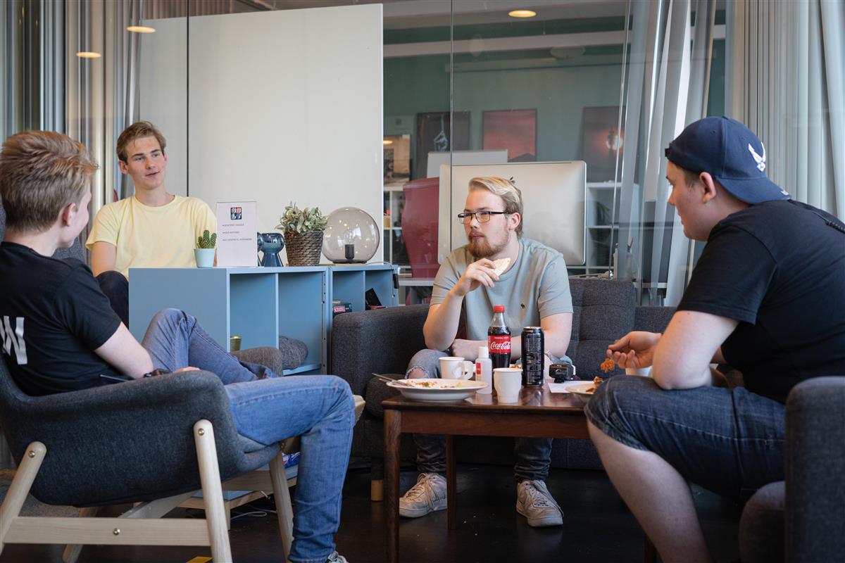 Fire unge menn sitter i en kafé med de spiser mat og samtaler  - Klikk for stort bilde