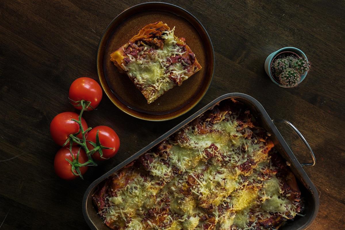 Lasagne i en ildfast form, tomater og et stykke lasagne på en tallerken - Klikk for stort bilde