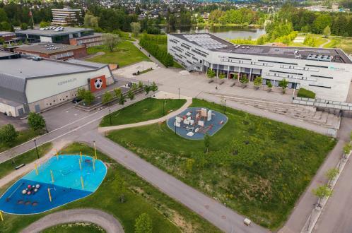 Dronefoto som viser Kjennhallen, Mailand videregående skole og aktivitetsparken i mellom - Klikk for stort bilde