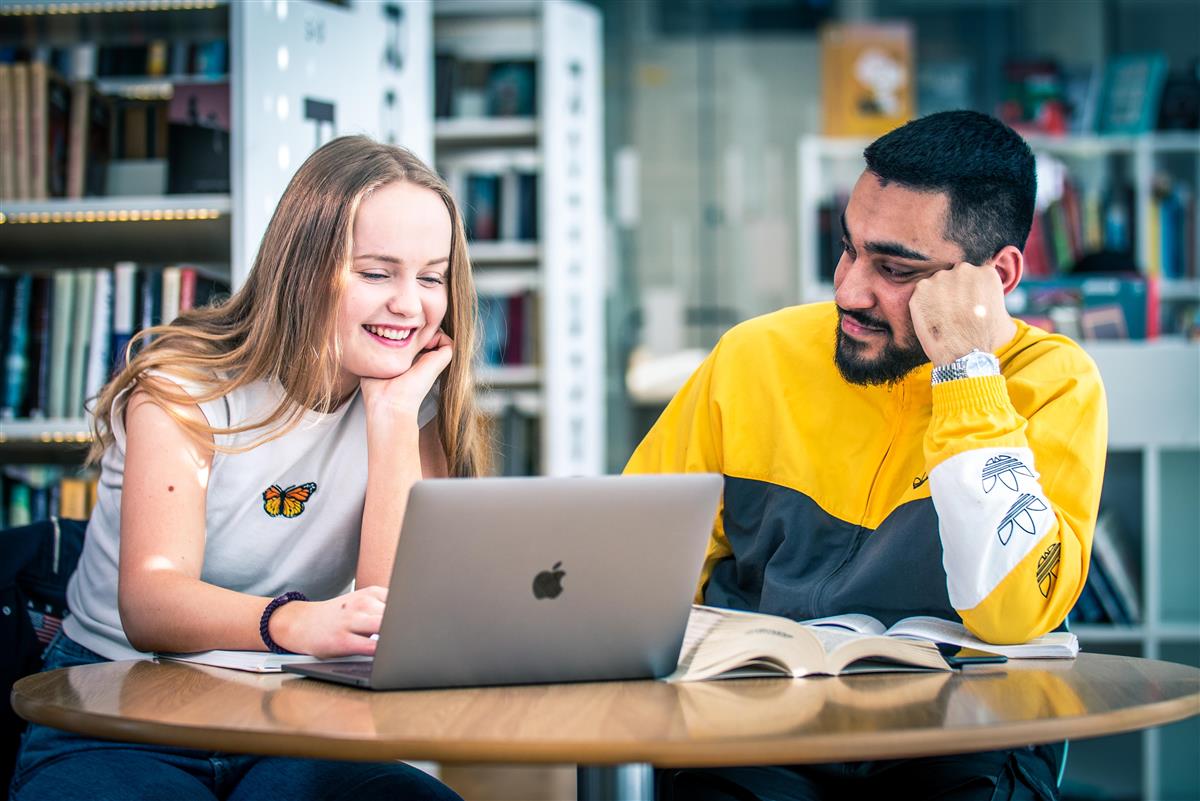 Jente og gutt sitter foran laptop på biblioteket - Klikk for stort bilde