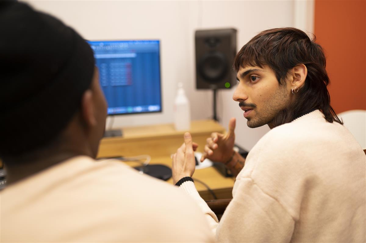 En ung mann i et musikkstudio forklarer noe til en annen person - Klikk for stort bilde